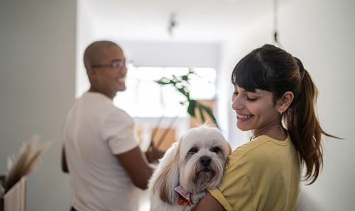 En kvinne med hund og mann bærer Alfa-flytteesker inn i den nye leiligheten sin.