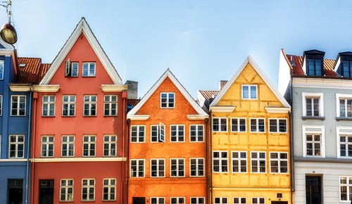 En række farverige etageejendomme i Danmark med en blå himmel, der viser lokale boligmuligheder.