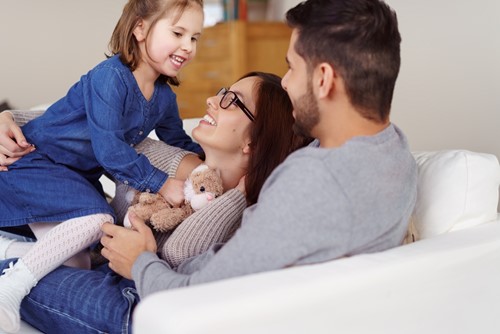 En närbild av en familj på tre som kramas i en vit soffa i sitt vardagsrum.