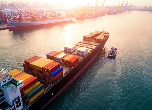 Et stort frakteskip frakter containere med flyttegods i havnen i solnedgang.