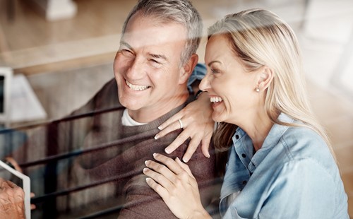 Smiliende, midaldrende par som sidder i deres dagligstue og er tilfredse med deres internationale flytning.