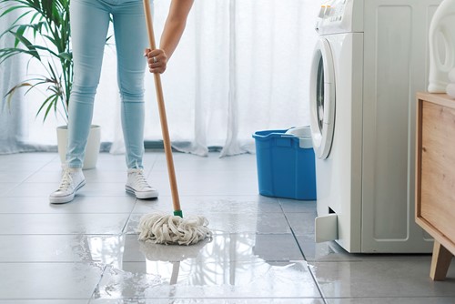 En närbild av en person som städar upp ett vattenläckage från en tvättmaskin i en lägenhet.