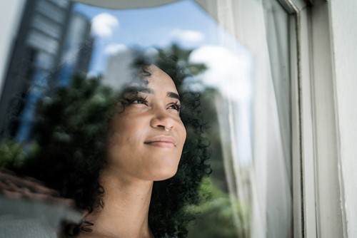 Et nærbilde av en afroamerikansk jente som ser ut av vinduet mot himmelen.