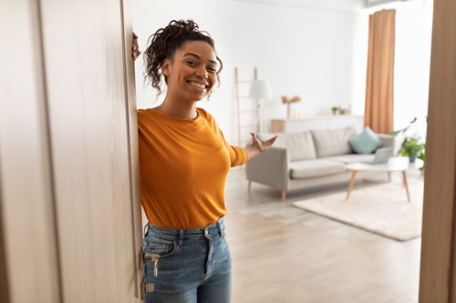 An african american woman greeting visitors by the doorway showing her apartment livingroom.