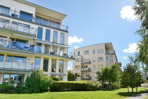An exterior of Scandinavian apartment buildings with balconys with a bright blue sky and greenery around.