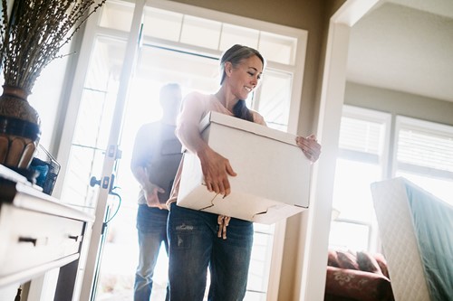 Couple holding Alfa boxes with Alfa logos entering their new house through the doorway.