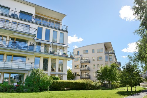 Exteriör av flerbostadshus med blå himmel och lite grönska som visar trevliga platser att bo på.