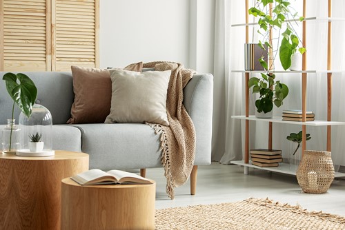 An interior from a livingroom with a sofa, table, shelf, plant etc in grey, beige, brown and green colors.
