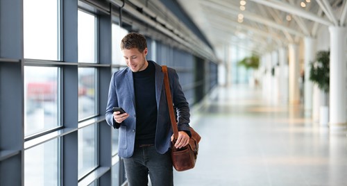 En forretningsmand kigger på sin mobil, mens han går gennem lufthavnen på vej til udlandet.