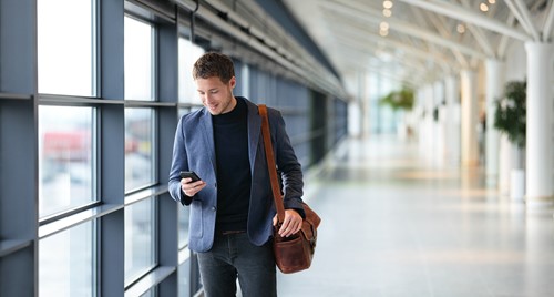 A business man looking at his mobile walking through the airport traveling abroad.