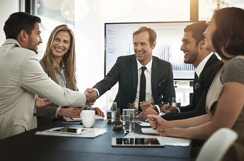 A group of business executives shaking hands sitting at a table in a conference room.