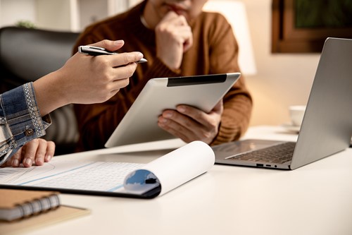 A close up of a landlord and a tenant sitting by a computer and signing a rental agreement in an office setting.