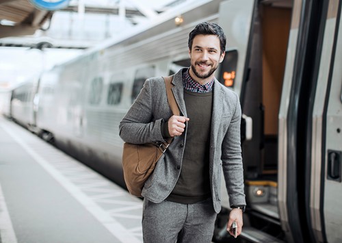 A male traveler holding his mobile and backpack at the train station.