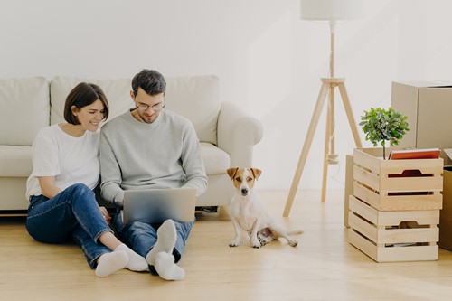 A couple sitting on the floor with their dog in their apartment looking at necessary documentation sent by the Alfa Move Coordinator.