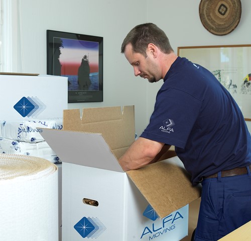 En Alfa-anställd i blå Alfa-kläder som packar i Alfa-flyttkartonger med blå Alfa-logga.