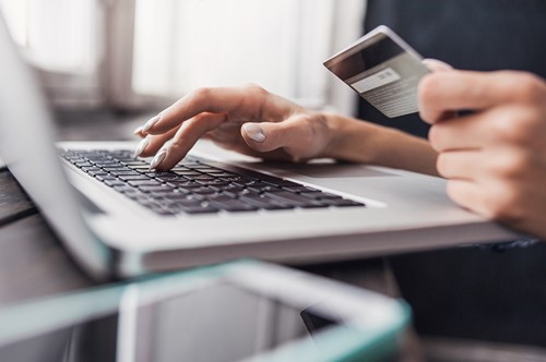 A close up of a persons hands holding a creditcard while typing on a computer.