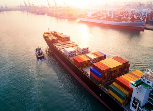 A container shipping vessel transporting household goods to a harbour in the sunset.