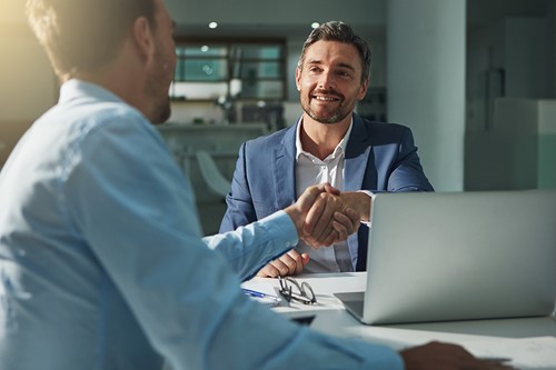 An Alfa consultant sitting at a desk at the office with a business customer shaking hands.