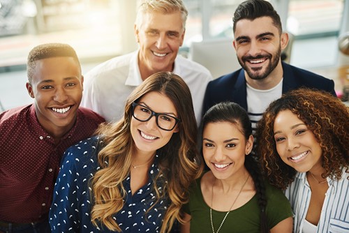 A diverse group of six people smiling at the camera in an office.