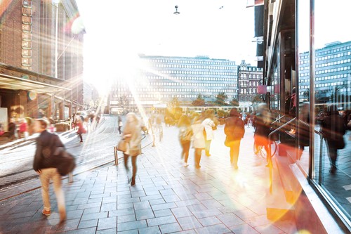 A bright city view of business buildings with blurred people walking the streets.